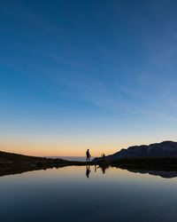 Silhouette man on lake against sky during sunset