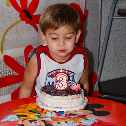 Boy blows a candle on his 3th birthday. burning candle in the form of the number 3. cake with candle