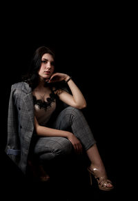 Portrait of young woman sitting against black background