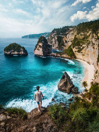 Man standing on rock at beach against sky