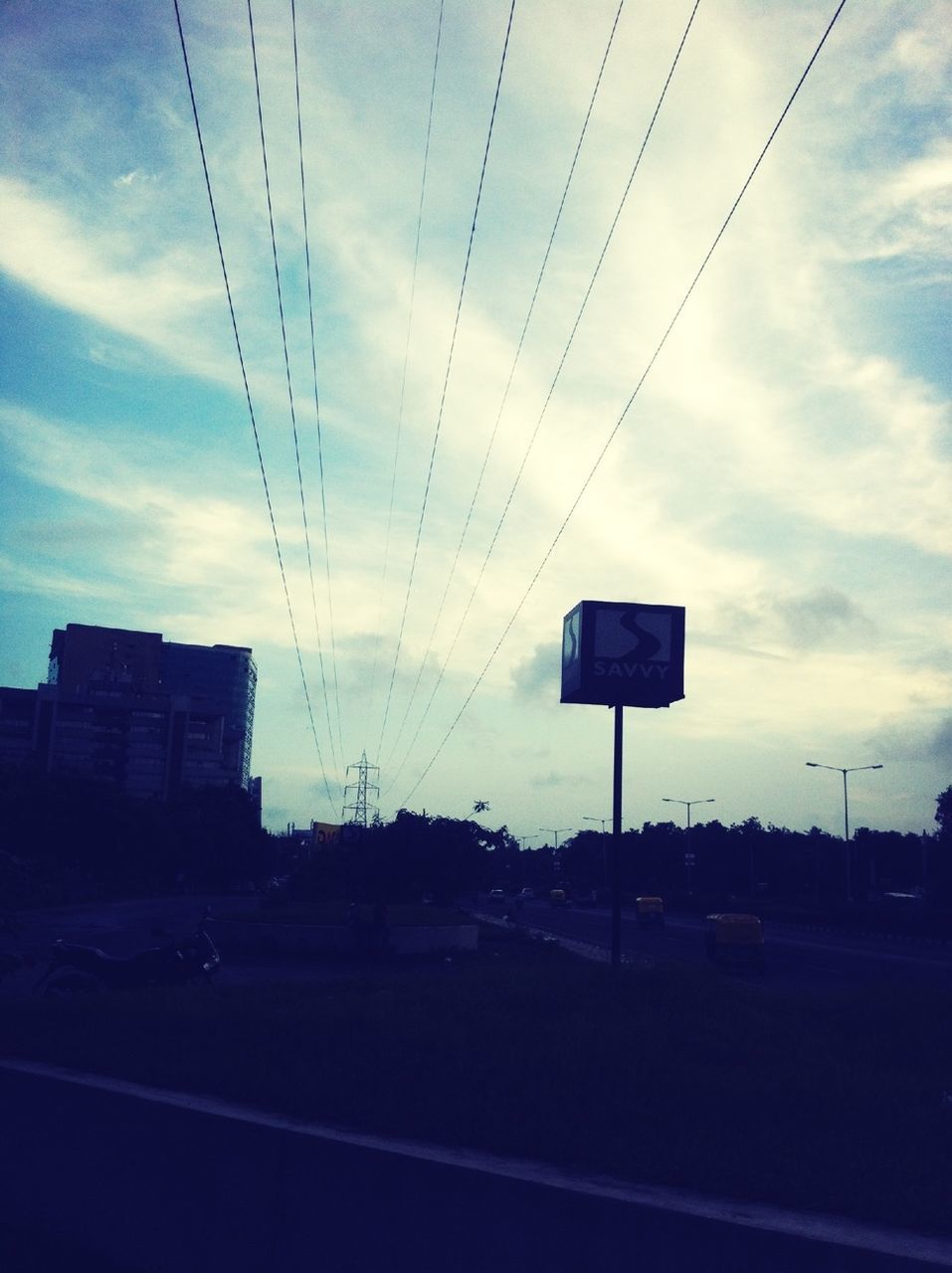 sky, power line, electricity pylon, transportation, road, street, electricity, cable, cloud - sky, road sign, communication, power supply, cloud, building exterior, built structure, street light, connection, tree, power cable, car