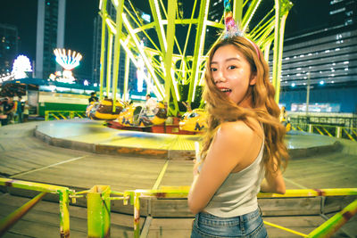 Portrait of young woman standing against chain swing ride