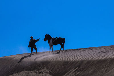 Man with horse on sand dune against clear blue sky