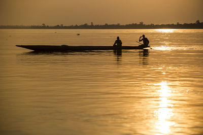 Silhouette men in sea against sky at sunset
