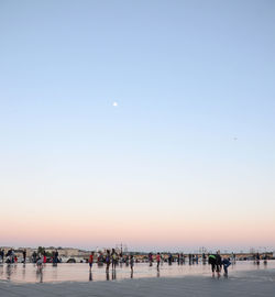 People on beach against clear sky during sunset