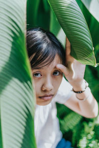 Close-up portrait of young woman sitting amidst plants in park