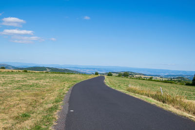 Empty road amidst field against sky