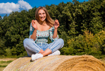 A young girl sits cross-legged on a hay bale and smiles