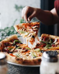 Cropped hand of woman holding pizza slice with server