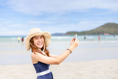 Portrait of smiling young woman taking selfie at beach