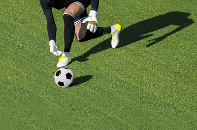 Low section of goalie running for soccer ball on field during sunny day