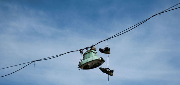 Low angle view of shoes hanging on cable against sky