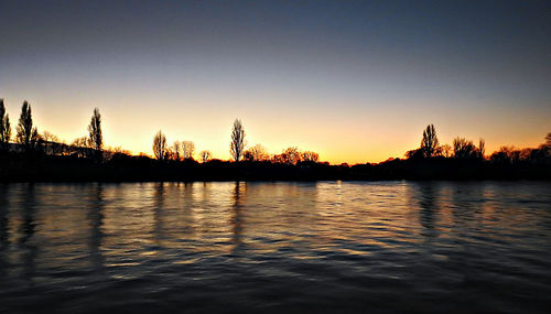 Silhouette trees by lake against clear sky during sunset