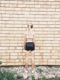 Rear view of girl standing against brick wall