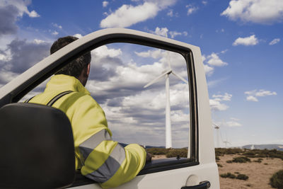 Technician looking at wind turbines standing by van door at wind farm