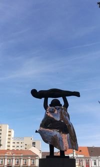 Low angle view of statue by building against sky