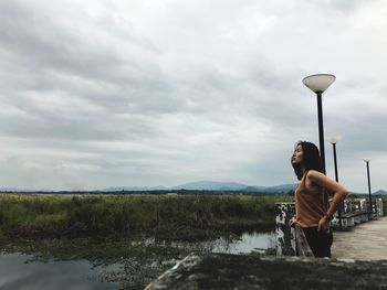 Side view of woman standing by lake against cloudy sky