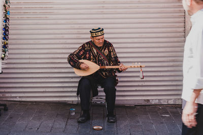 Full length of man playing guitar against wall