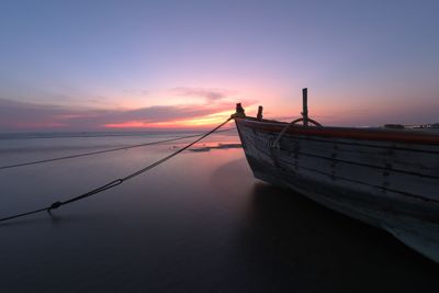 Boat moored in sea against sky during sunset