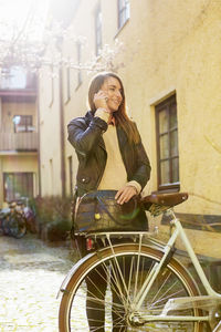 Businesswoman using smart phone while standing with bicycle on sidewalk