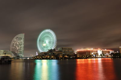 Illuminated city by river against sky at night