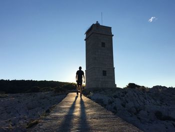 Silhouette man walking on jetty against clear blue sky