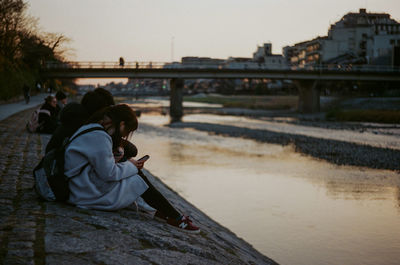 People sitting on bridge over river against sky