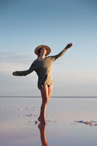 Attractive young caucasian woman in a straw hat and long jacket walks balancing on a shallow