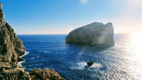 Rock formation in sea against clear blue sky