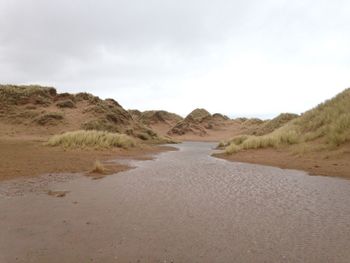 Dirt road by sand dune against sky