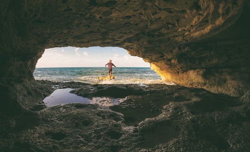 Man standing on rock by sea against sky