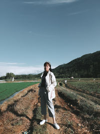 Full length portrait of young woman standing on field against sky