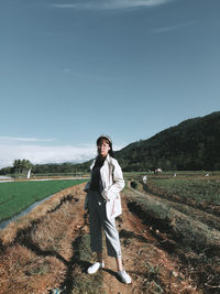 Full length portrait of young man standing on field against sky