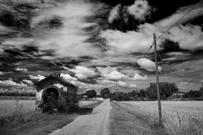 Road passing through field against cloudy sky