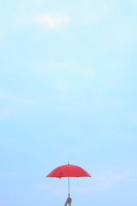 Cropped hand holding umbrella against sky