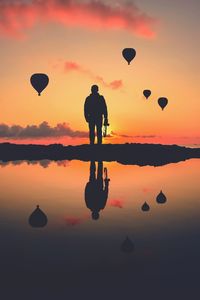 Silhouette of hot air balloons and man reflecting on sea during sunset