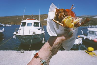 Cropped hand holding food at harbor on sunny day