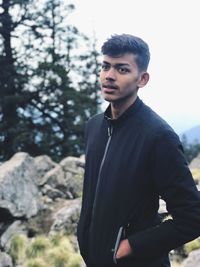 Young man looking away while standing outdoors