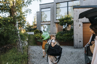 Boys with luggage walking on driveway towards modern villa