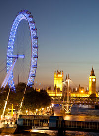 Illuminated ferris wheel in city against sky at night