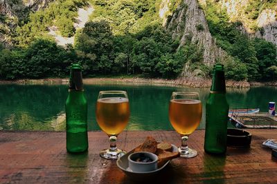 Wine glasses on table by lake against trees