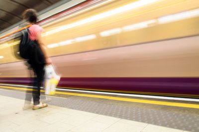 Blurred motion of train moving by woman standing at subway station