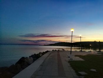 Road by sea against sky at sunset