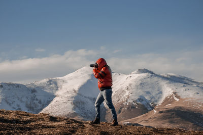 Man with camera taking photos on snowcapped mountain against sky