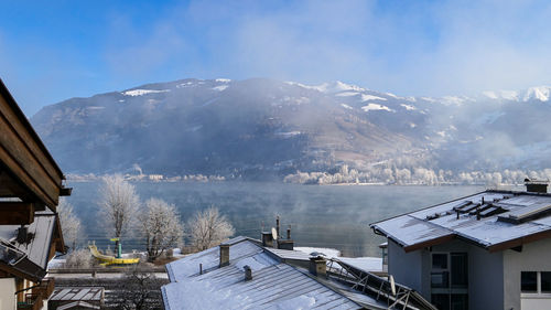 Winter house roofs and misty surface of zell am see lake in sunny alps of austria