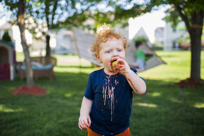 Cute baby boy eating ice cream while standing on grassy field at yard