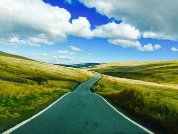 High angle view of empty road amidst grassy field against cloudy sky