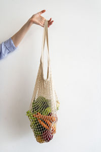 Woman holding vegetables inside mesh bag in front of wall