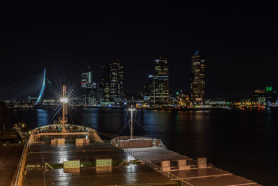 Illuminated buildings by river against sky at night