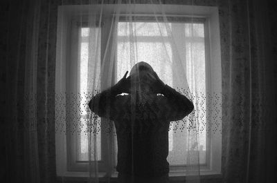 Rear view of woman standing by window at home